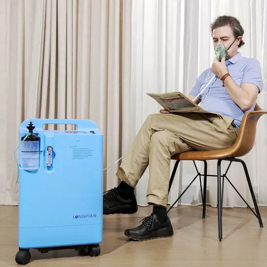 Blue Dynmed Elite oxygen concentrator on wheels with flow meter and humidifier bottle, next to seated man using nasal